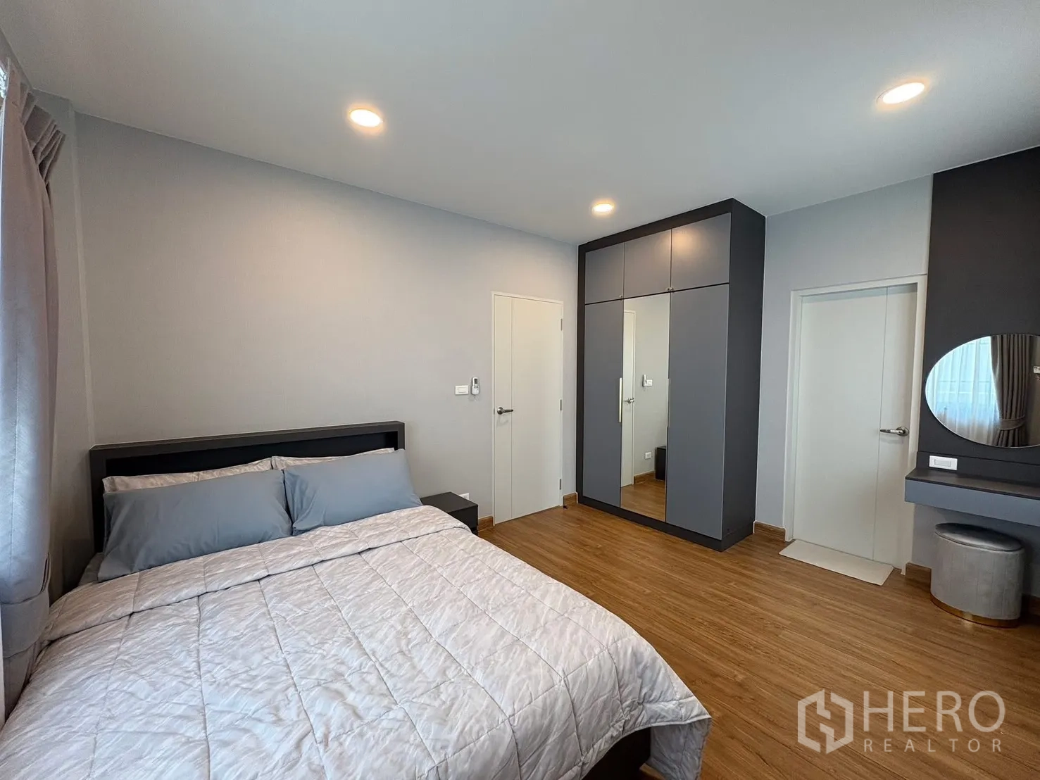 Detached House for rent in Bang Phli, Samut Prakan - Bedroom with grey bedding, mirrored wardrobe and dressing table set against warm wood floors.