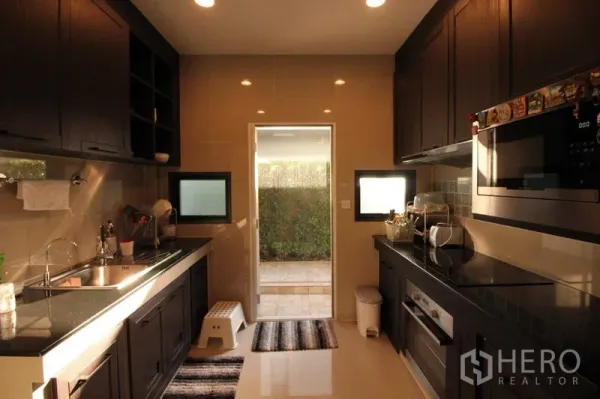 独立式住宅 出租在Prawet, Bangkok - 廊式厨房，深色橱柜与嵌入式电器，通向花园的门。