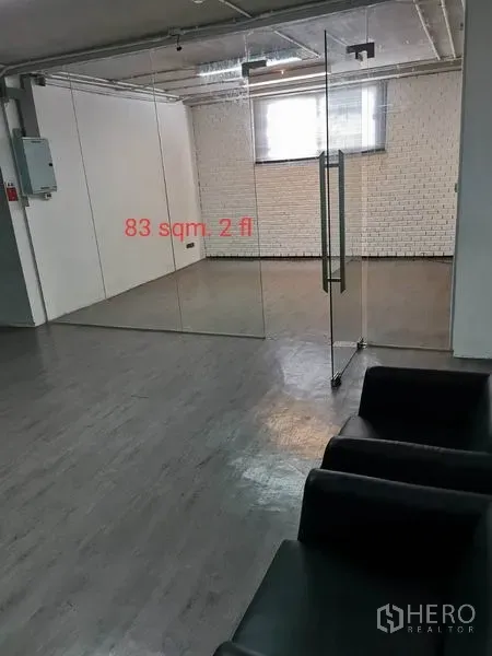Office Space for rent in Khlong Toei, Bangkok - Glass-partitioned meeting room inside an open office, featuring grey floors, white brick wall, window and nearby black seating.