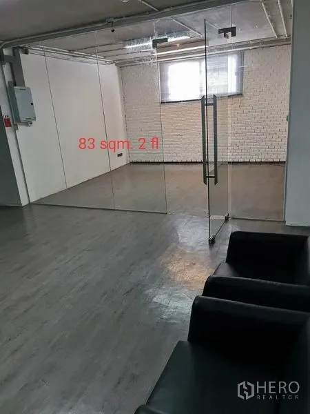 Office Space for rent in Khlong Toei, Bangkok - Glass-partitioned meeting room inside an open office, featuring grey floors, white brick wall, window and nearby black seating.