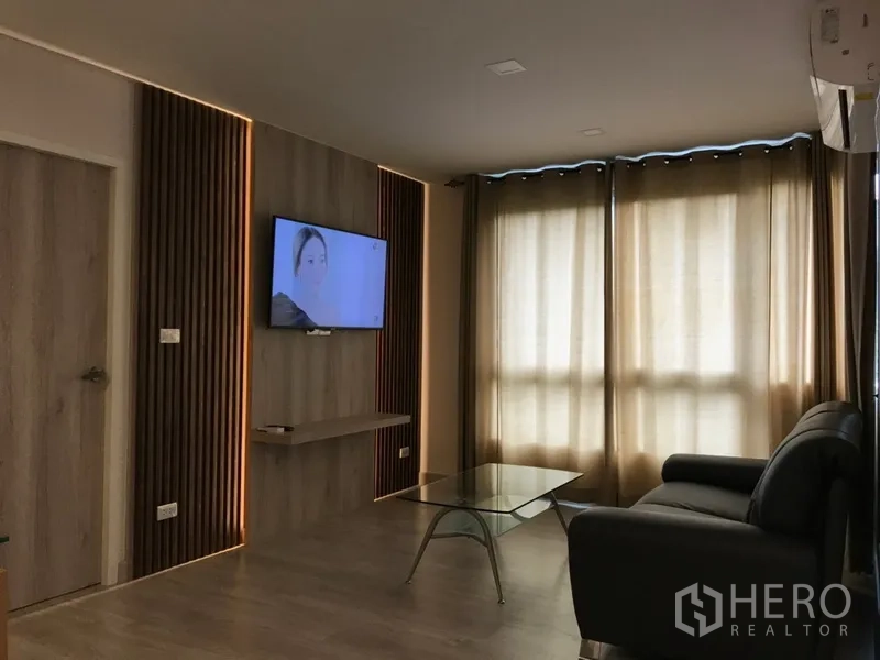 คอนโด ให้เช่าในWatthana, Bangkok - ห้องนั่งเล่นอบอุ่น โซฟาหนัง ทีวีติดผนัง และหน้าต่างบานใหญ่พร้อมม่านทึบ