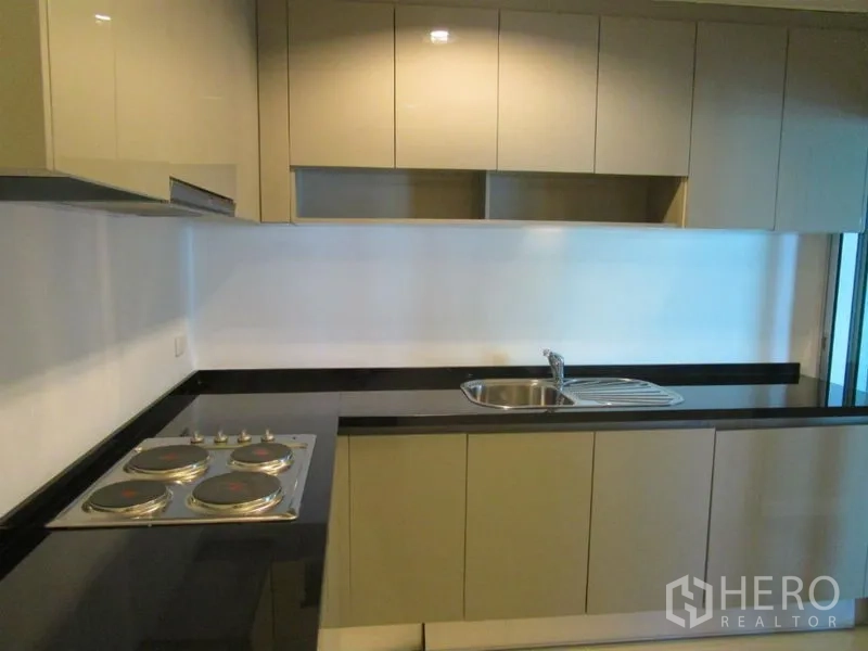 Condominium for sale in Huai Khwang, Bangkok - Modern kitchen with black stone countertops, electric cooktop, and upper cabinets