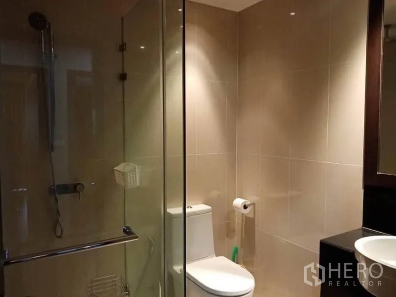 公寓 出租在Sathon, Bangkok - 米色瓷砖浴室，玻璃淋浴间与坐便器。