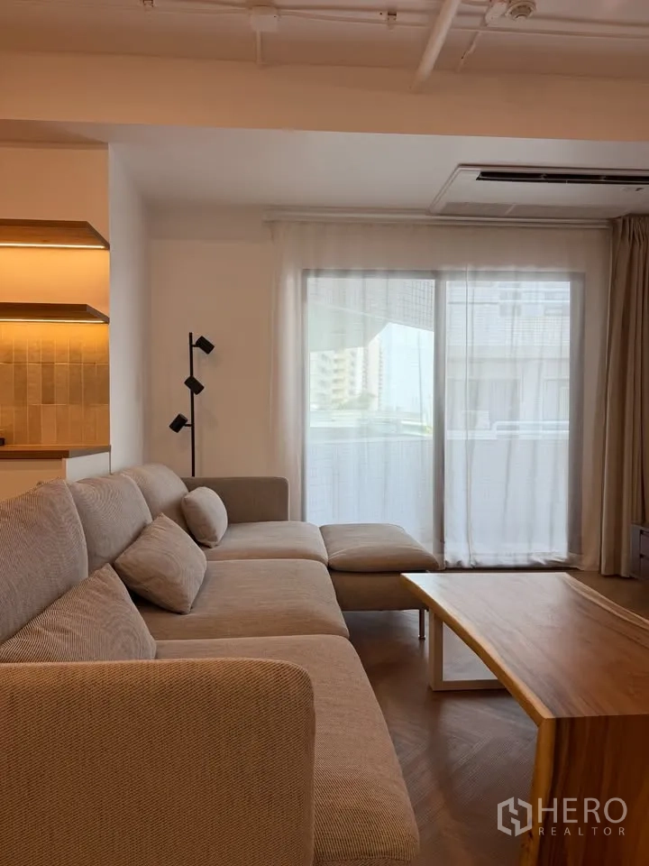 Condominium for rent in Watthana, Bangkok - Bright living room with L-shaped sofa, wood coffee table, and balcony door.