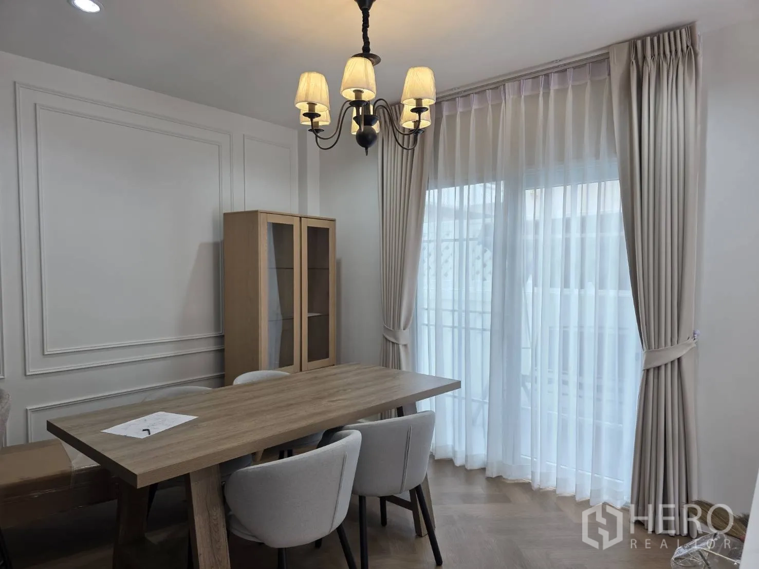 Detached House for sale in Lam Luk Ka, Pathum Thani - Dining area with wooden table, upholstered chairs, tall display cabinet, and floor-to-ceiling curtains.