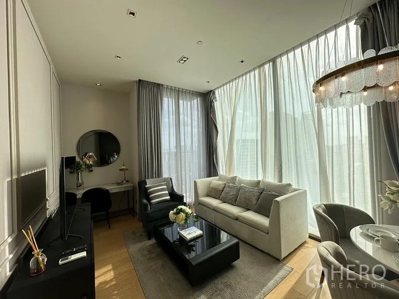 Condominium for rent in Pathum Wan, Bangkok - Open-plan lounge with floor-to-ceiling curtains, sofa and daylight filtering through tall windows.