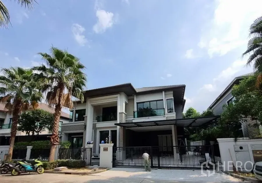 Detached House for rent in Bang Khae, Bangkok - Street view of the gated two-storey house framed by palm trees in Bang Khae.