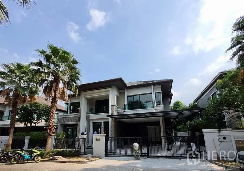 Detached House for rent in Bang Khae, Bangkok - Street view of the gated two-storey house framed by palm trees in Bang Khae.