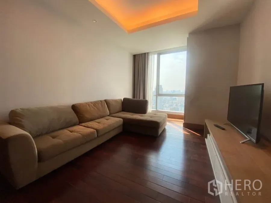 公寓 出租在Sathon, Bangkok - 明亮客厅，L型沙发、木地板与落地窗，眺望曼谷天际线。