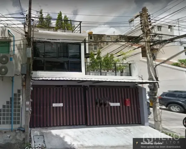 Townhouse for rent in Watthana, Bangkok - Modern two-storey townhouse exterior in Ekkamai with a wide sliding gate, large glass windows, and a rooftop terrace with greenery along a quiet lane.