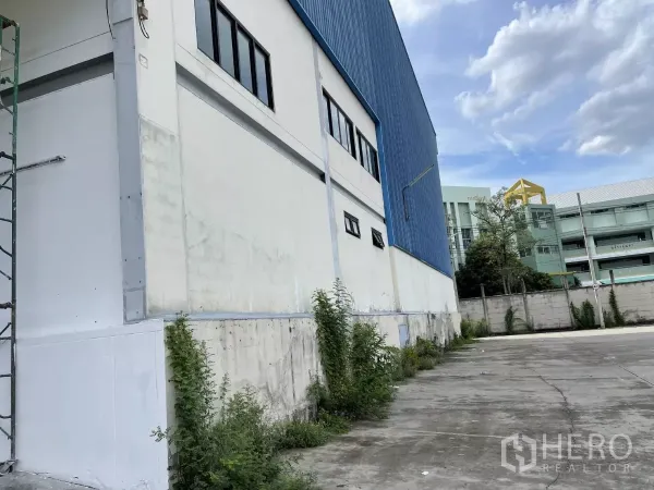 Warehouse for rent in Lat Krabang, Bangkok - Side elevation of the warehouse with a concrete driveway and nearby buildings.