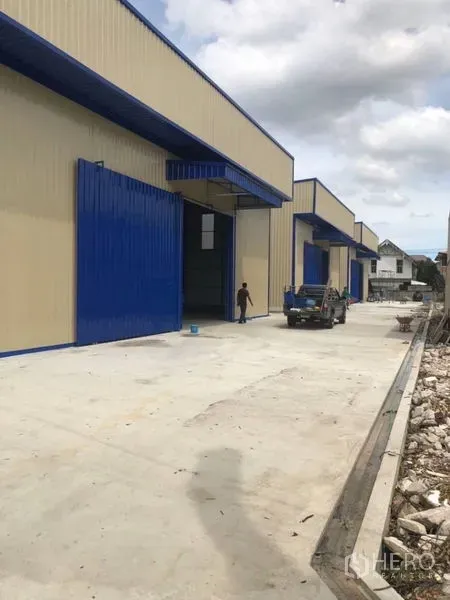 Warehouse for rent in Wang Thonglang, Bangkok - Modern row of warehouses with blue doors and a wide concrete driveway for loading and parking.