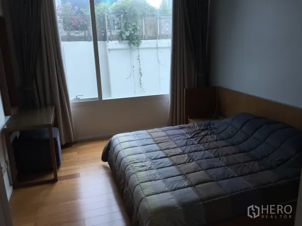 Condominium for sale in Watthana, Bangkok - Cozy bedroom with wood flooring, a large window with curtains, desk, and double bed.