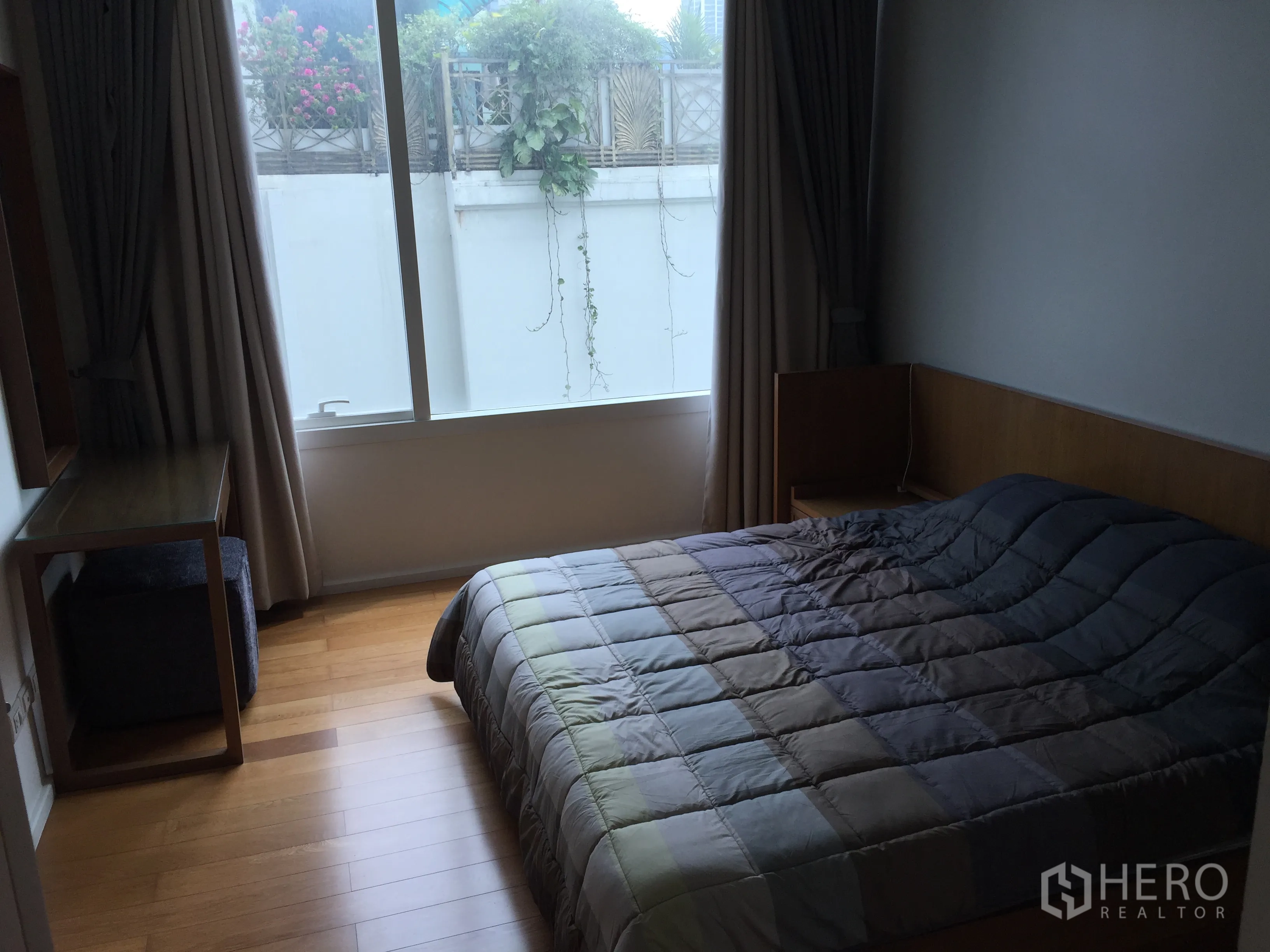 Condominium for sale in Watthana, Bangkok - Cozy bedroom with wood flooring, a large window with curtains, desk, and double bed.