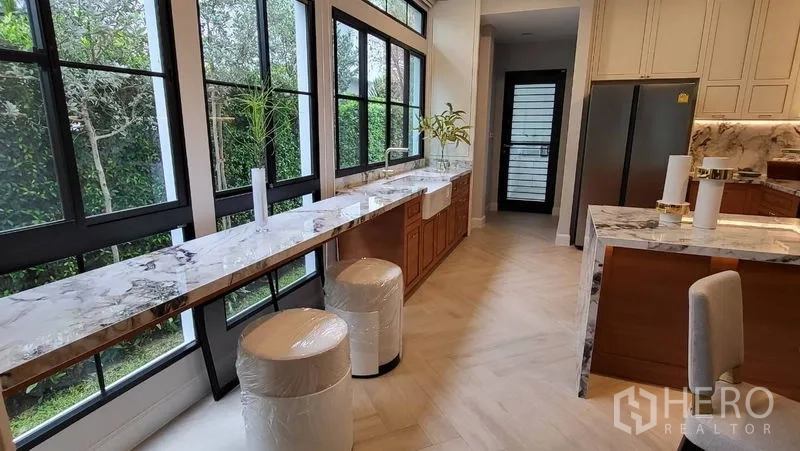 Detached House for rent or sale in Saphan Sung, Bangkok - Light-filled kitchen with long marble breakfast bar and garden views through tall windows.