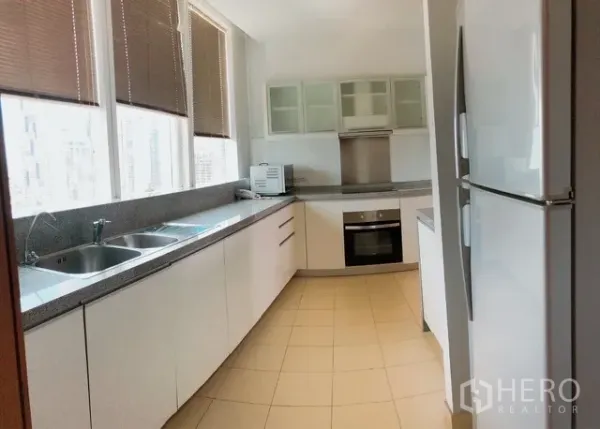 Condominium for rent or sale in Khlong Toei, Bangkok - Long galley kitchen with granite countertops, double sink, tall windows with blinds, full-size fridge and built-in oven.