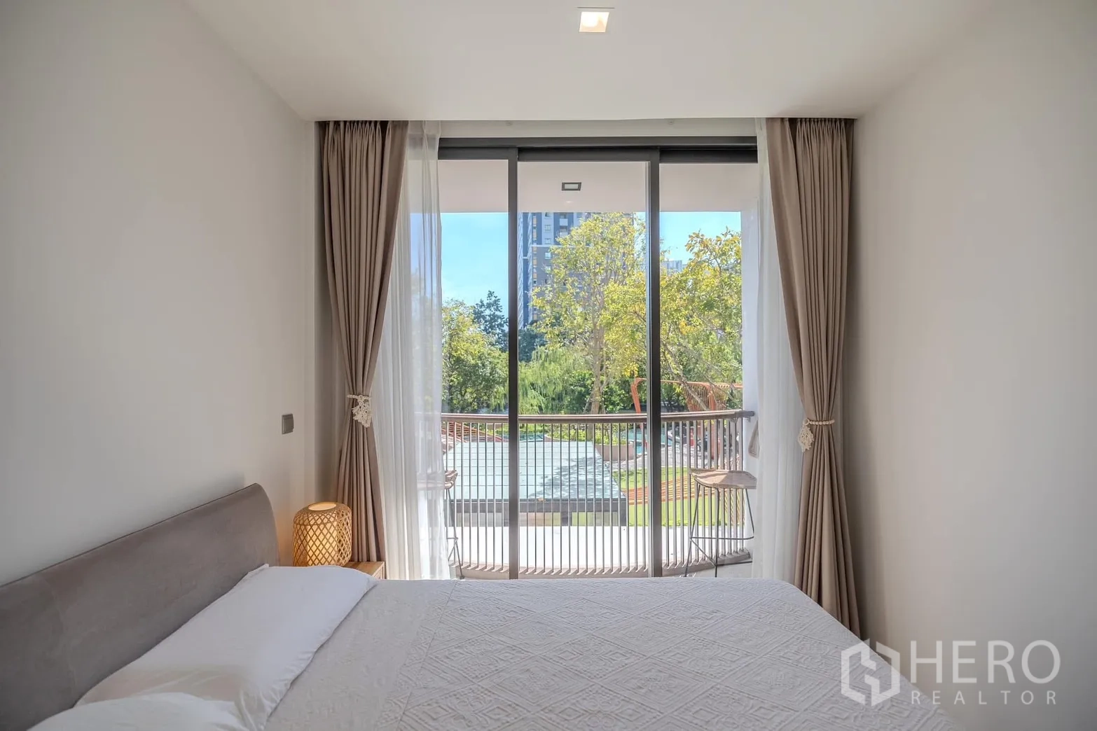 Condominium for rent in Watthana, Bangkok - Bed facing sliding glass doors to a balcony with a garden view.