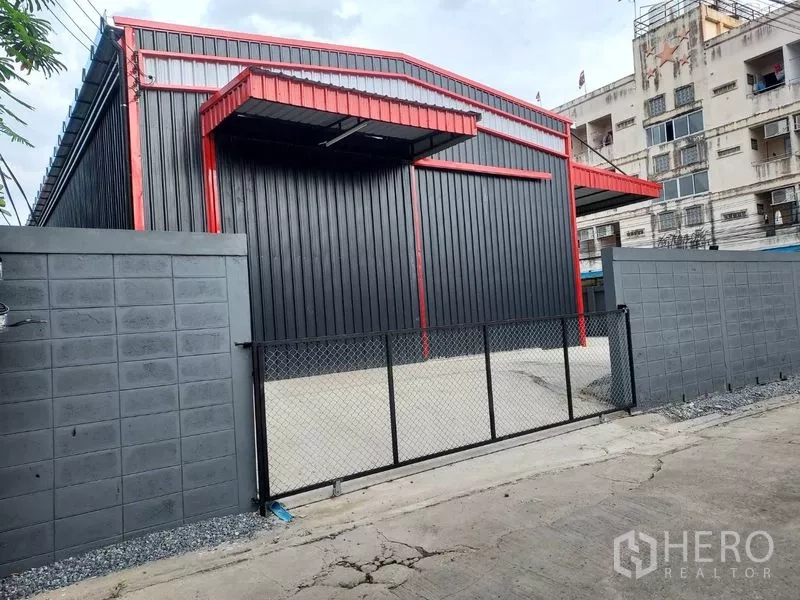 คลังสินค้า ให้เช่าในBang Kapi, Bangkok - ด้านนอกโกดังโครงเหล็กหลังคาจั่ว สีดำตัดแดง พร้อมประตูรั้วและลานคอนกรีต
