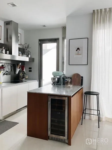 Detached House for sale in Bang Kapi, Bangkok - Kitchen island with marble top, wine cooler, and stool beside a glass door.
