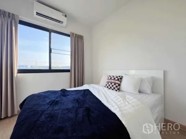 Townhouse for rent in Min Buri, Bangkok - Sunlit bedroom with double bed, air-conditioner, and large window with beige curtains.