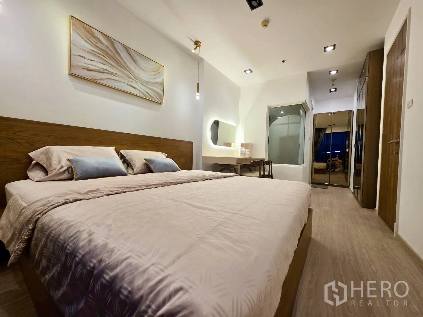 Condominium for rent in Huai Khwang, Bangkok - Bedroom with king bed, wood headboard, vanity desk, and glass partition to the bathroom.