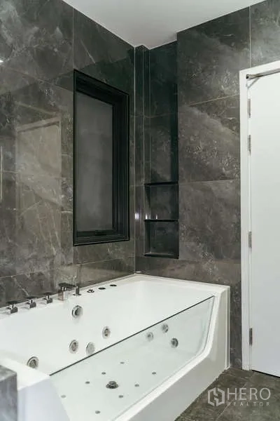 บ้าน ขายในSai Mai, Bangkok - ห้องน้ำกรุหินอ่อนพร้อมอ่างจากุซซี่สีขาวและหน้าต่างกรอบดำ