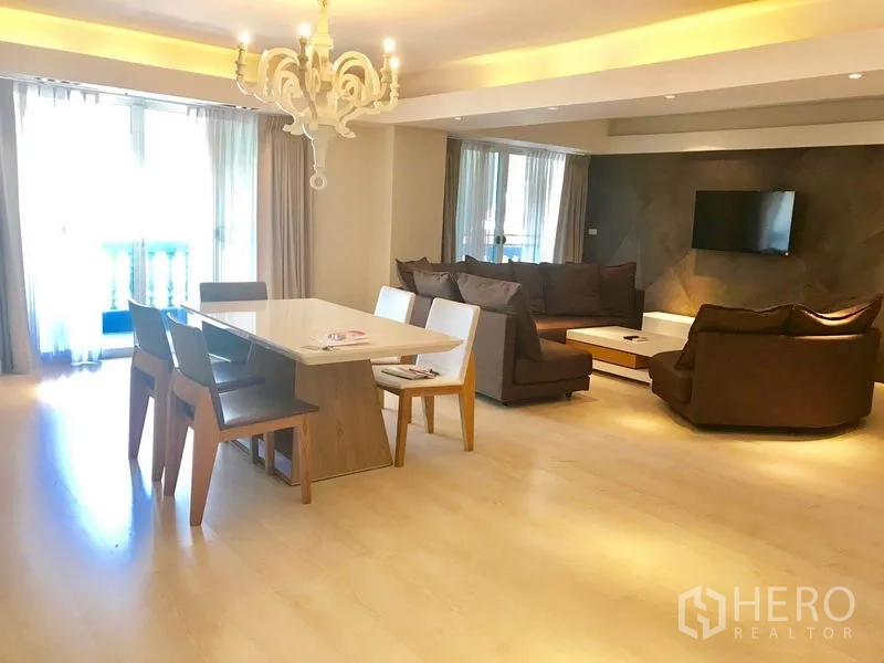 Condominium for rent or sale in Watthana, Bangkok - Bright open-plan living and dining area with chandelier, brown sofas, and floor-to-ceiling windows.