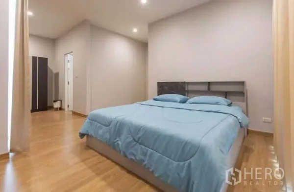 独立式住宅 出租或出售在Lat Phrao, Bangkok - 宽敞卧室，木地板、筒灯与蓝色床品。