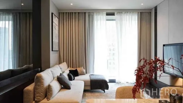 Condominium for rent or sale in Watthana, Bangkok - Bright living room with L-shaped sofa, TV wall, floor-to-ceiling curtains and balcony light.