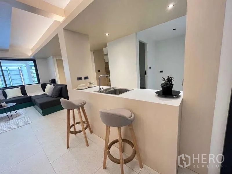 Townhouse for sale in Khlong Toei, Bangkok - Kitchen peninsula with sink and two bar stools facing the living area.