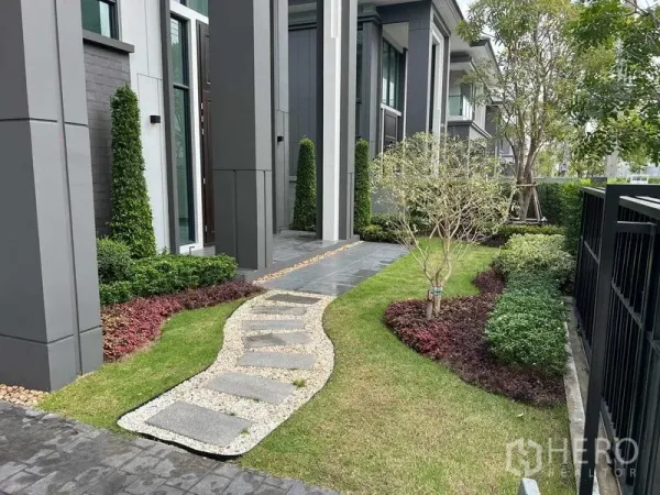 Detached House for rent in Khlong Sam Wa, Bangkok - Landscaped side garden with curved stepping-stone path, manicured shrubs and tall columns.