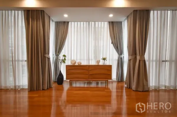 คอนโด ให้เช่าในPathum Wan, Bangkok - มุมห้องกระจกกว้าง ม่านสีเทา พร้อมตู้ลิ้นชักไม้บนพื้นไม้เงางาม