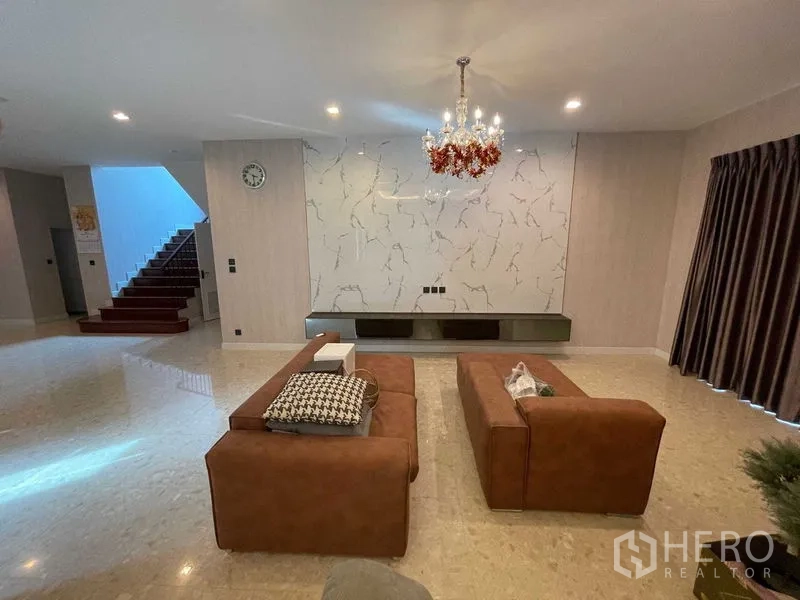 Detached House for sale in Mueang Samut Prakan, Samut Prakan - Spacious living room with marble feature wall, chandelier and matching brown sofas.