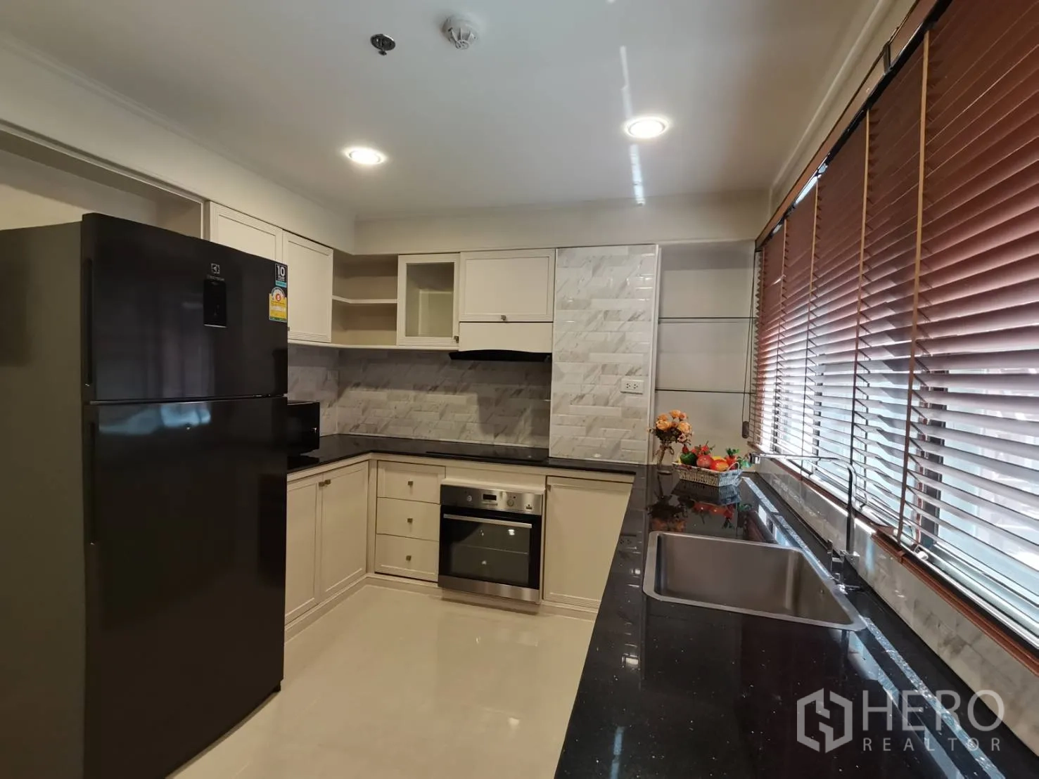 อพาร์ทเมนท์ ให้เช่าในWatthana, Bangkok - ครัวรูปตัวแอล เคาน์เตอร์หินแกรนิตสีดำ เตาอบ เครื่องดูดควัน และตู้เย็นขนาดใหญ่ ใต้บานมู่ลี่