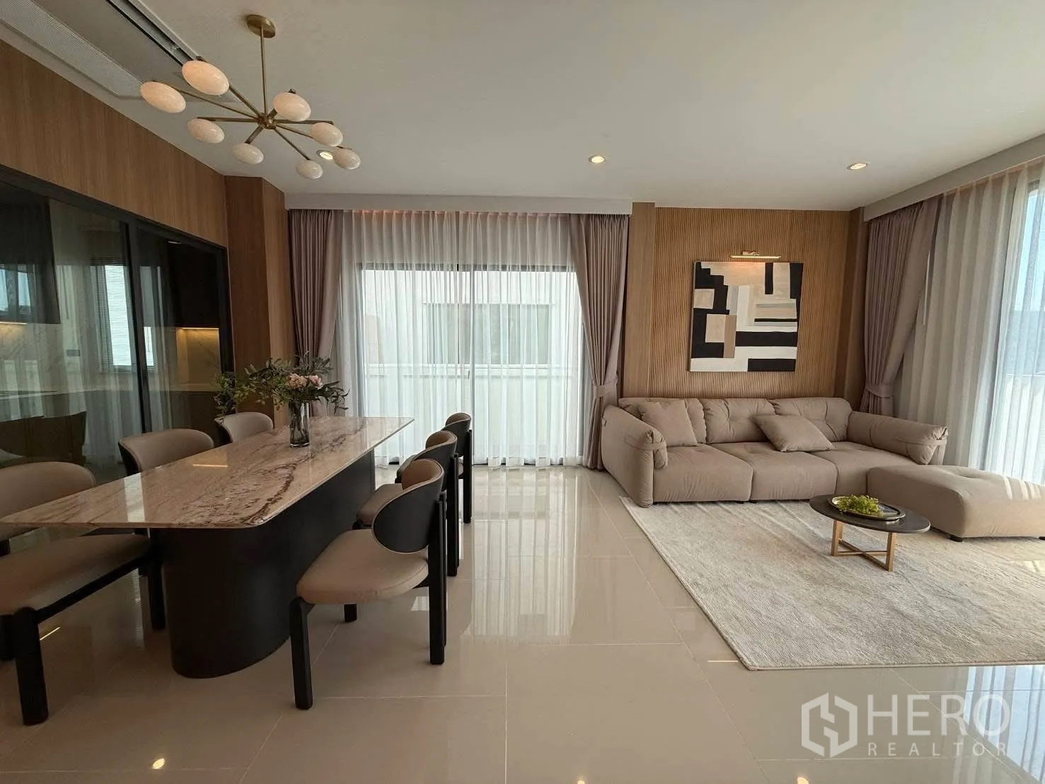 Detached House for rent in Bang Phli, Samut Prakan - Open-plan living and dining area with a marble dining table, pendant light, L-shaped sofa, and large windows.