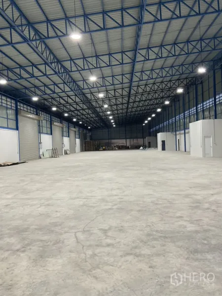 Warehouse for rent in Bang Bua Thong, Nonthaburi - Open-span interior with smooth concrete floor, ample lighting, and small side office rooms.