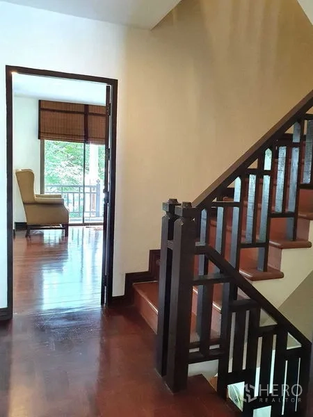 Townhouse for rent or sale in Suan Luang, Bangkok - Staircase with dark wood handrail opening to a bright room and balcony.
