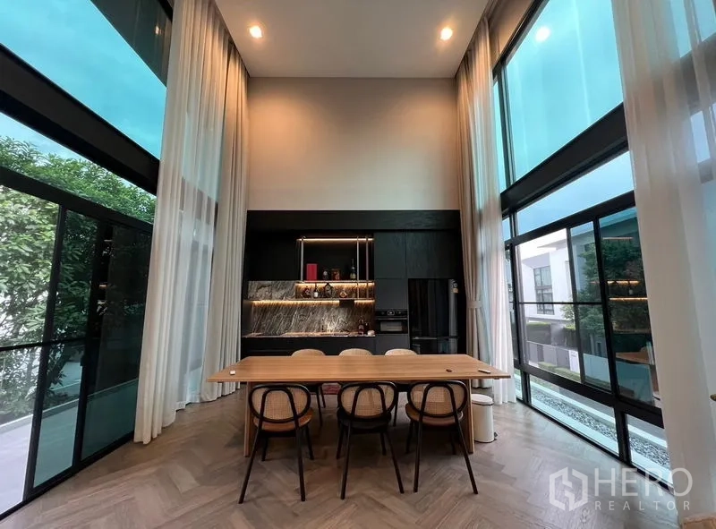 Detached House for sale in Saphan Sung, Bangkok - Double-height dining space with sleek black kitchen, marble backsplash and tall glass walls.