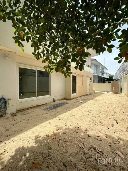 独立式住宅 出售在Prawet, Bangkok - 阳光后院，沙地铺设，白色外墙与推拉落地窗。