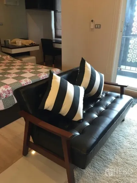 คอนโด ให้เช่าในWatthana, Bangkok - โซฟาหนังสีดำพร้อมหมอนลายทาง ข้างประตูกระจกบานเลื่อนออกไประเบียงและเตียง