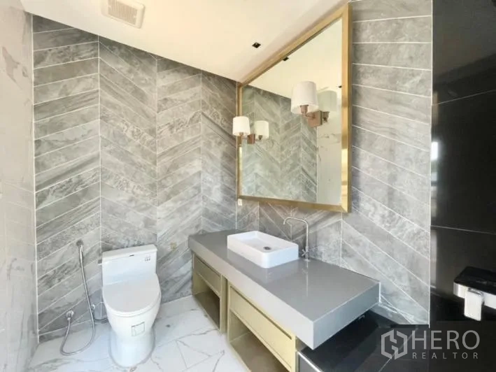Detached House for rent or sale in Khlong Toei, Bangkok - Designer bathroom featuring a herringbone tile wall, large gold-framed mirror and vessel sink.