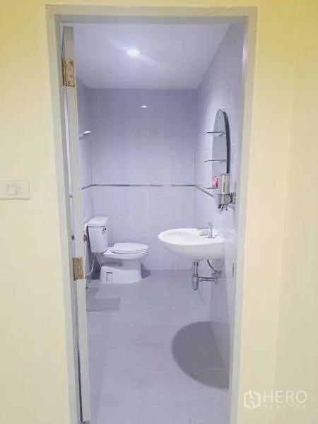 货栈 出租在Mueang Samut Prakan, Samut Prakan - 从门口看到的浅灰瓷砖卫生间，设洗手盆、镜子和坐便。