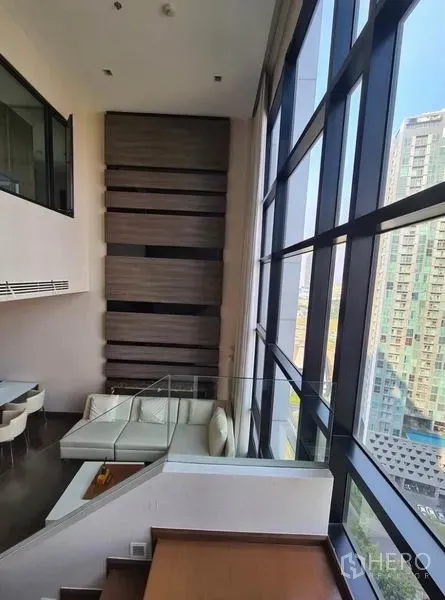 Condominium for rent or sale in Huai Khwang, Bangkok - View from stairs to mezzanine beside full-height glass wall overlooking skyline.