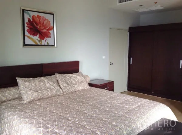 Condominium for rent or sale in Watthana, Bangkok - Master bedroom with a large bed, bedside tables and a dark wood wardrobe.
