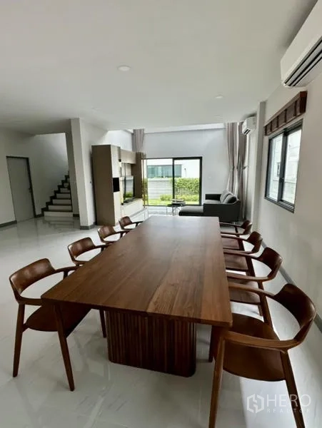 独立式住宅 出租在Bang Phli, Samut Prakan - 开放式用餐区在楼梯旁，木桌与八把同款椅子。