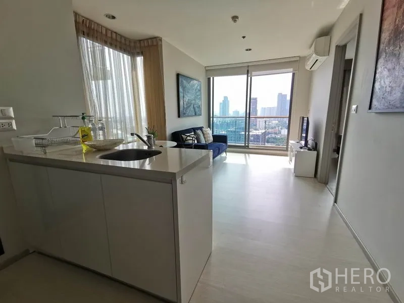 Condominium for rent in Khlong Toei, Bangkok - Kitchen island looking toward a bright living room with large windows and balcony.