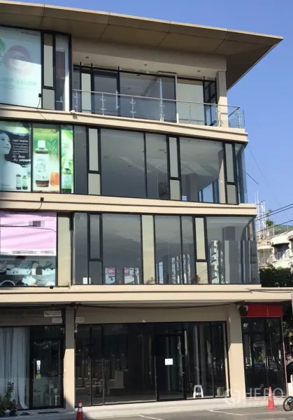 零售空间 出租在Suan Luang, Bangkok - 现代多层商业楼，整面落地玻璃店面，楼上带阳台，前方有停车区，晴朗天空下