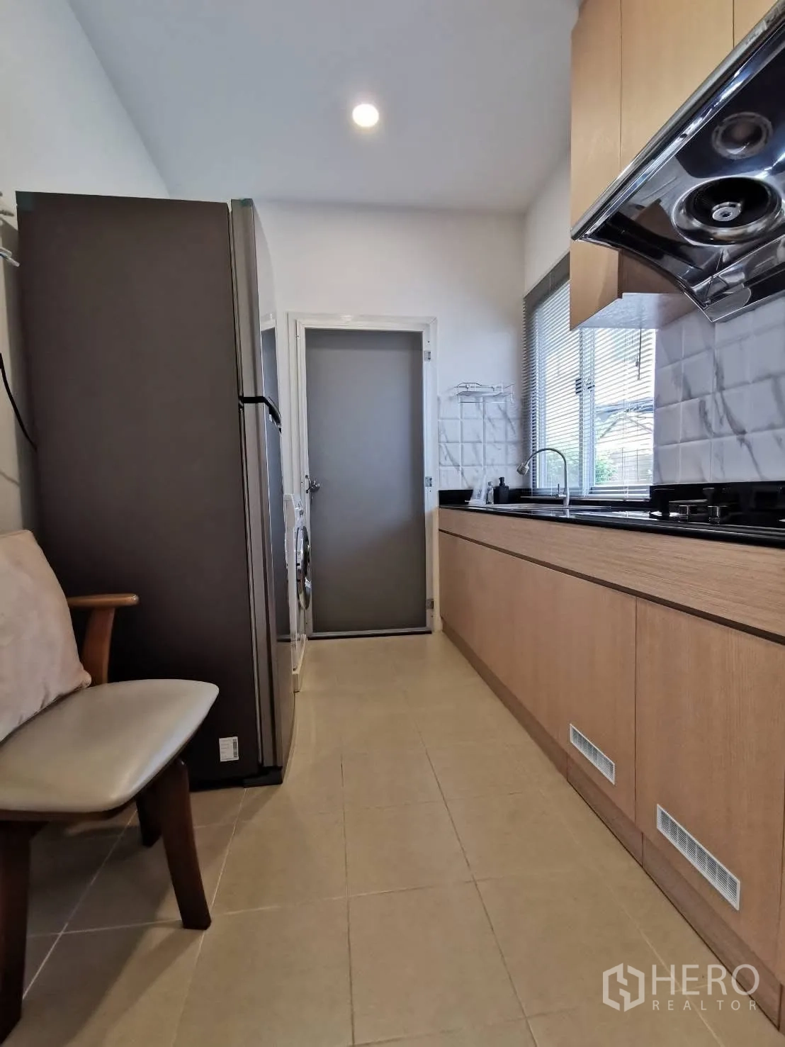 Detached House for rent in Bang Phli, Samut Prakan - Galley kitchen with light wood cabinets, black countertop, range hood, refrigerator, and washing machine.