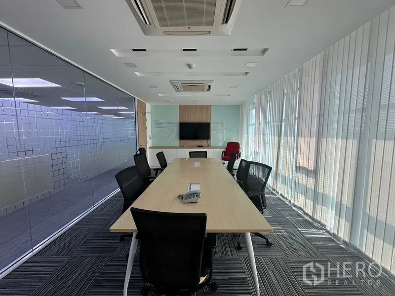 Office Space for rent - Glass-walled boardroom with long meeting table, ceiling AC, TV display, and whiteboard.