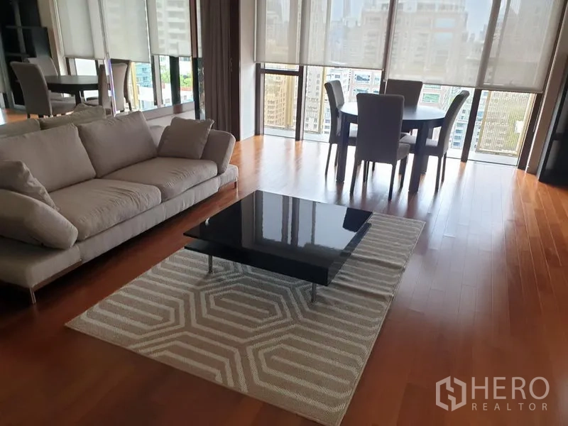 คอนโด ให้เช่าในPathum Wan, Bangkok - ห้องนั่งเล่นสว่าง โซฟา โต๊ะกลางสีดำบนพรม พร้อมชุดทานข้าว และหน้าต่างพาโนรามาวิวกรุงเทพฯ